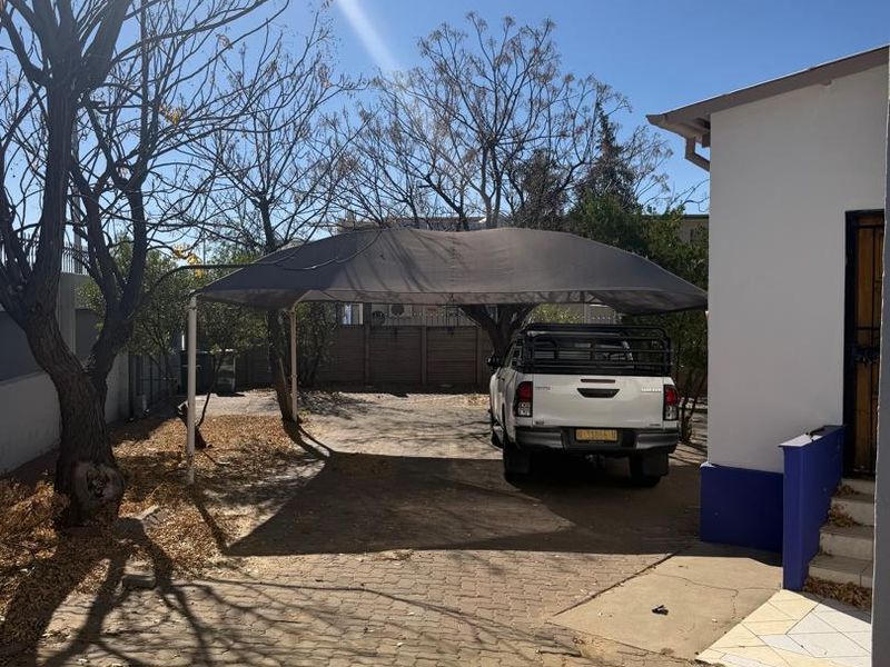 Rear exterior area featuring a paved driveway, a shade cloth carport structure, and perimeter walling.