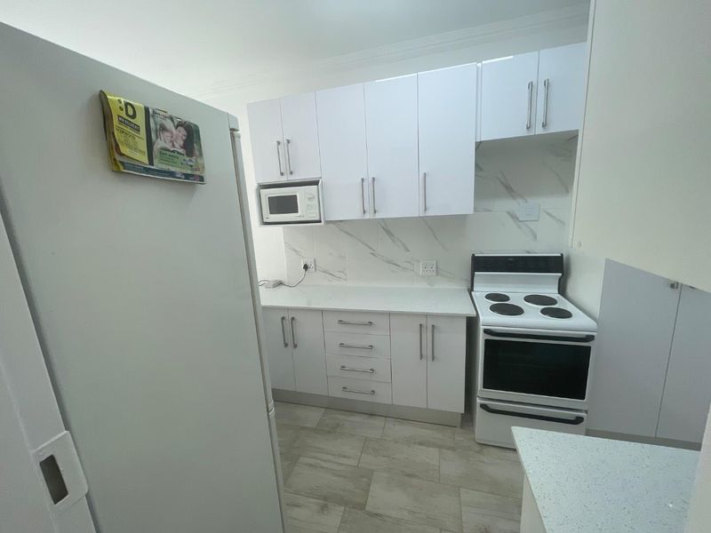A modern, clean kitchen featuring white cabinetry, stone countertops, marble-look backsplash, and a freestanding electric stove.