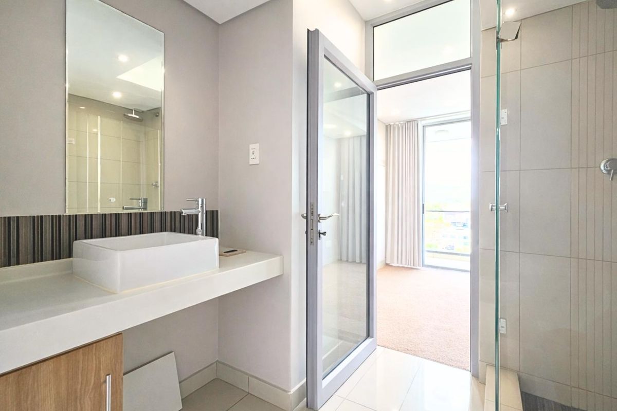 Modern bathroom featuring a vessel sink, vanity cabinet, wall mirror, and a glass-enclosed shower with neutral tiling.