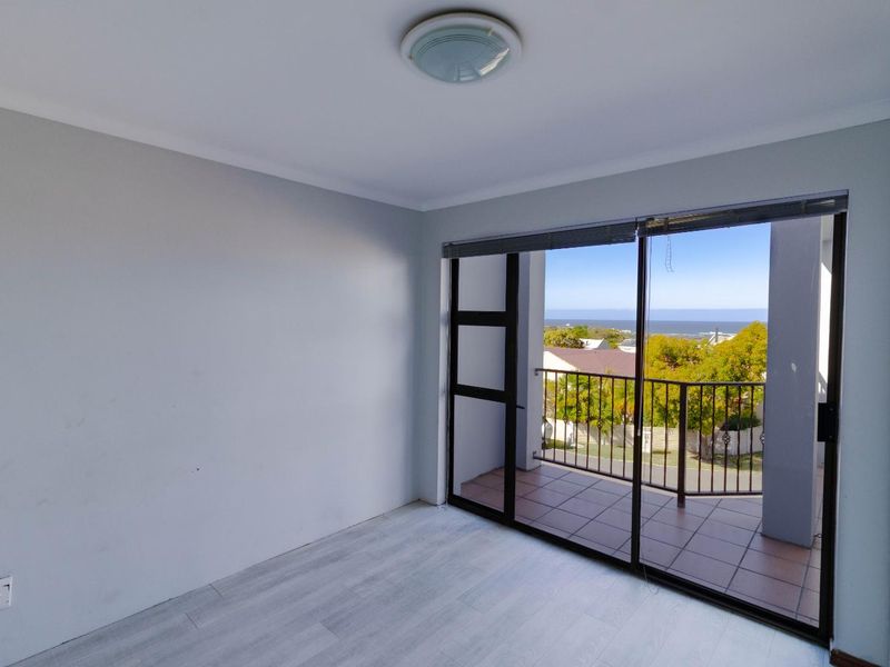 An empty bedroom featuring light laminate flooring, a ceiling light, and sliding glass doors that open onto a balcony with scenic views.