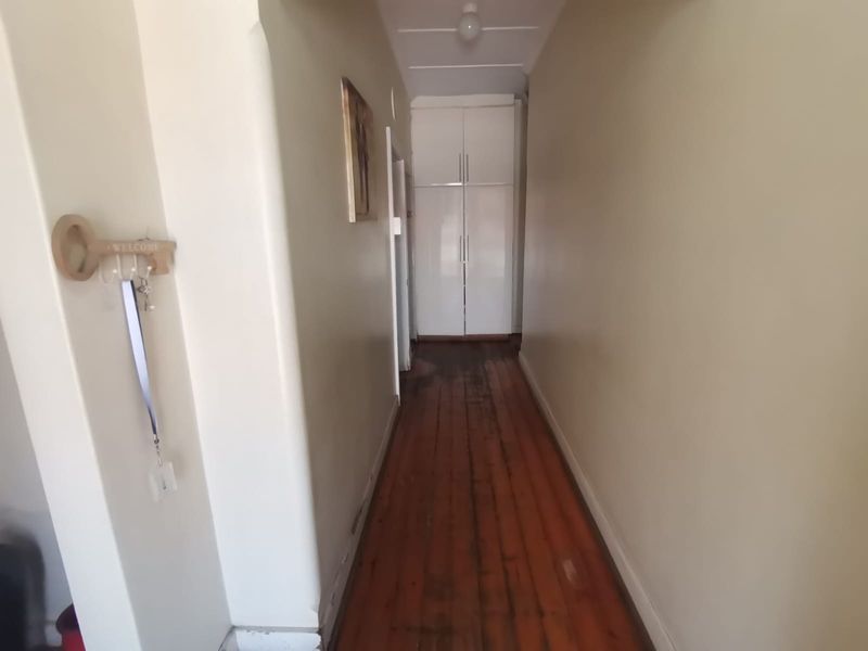 A narrow hallway featuring original timber flooring and a built-in storage cupboard at the end.