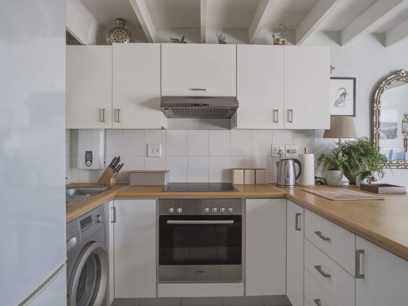 A compact, well-maintained kitchen featuring white cabinetry, wooden countertops, built-in oven and hob, and exposed ceiling beams.
