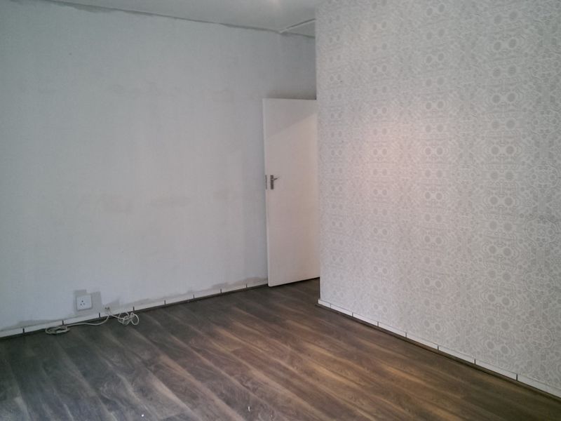 An empty office space featuring dark laminate flooring and a patterned feature wall, currently requiring finishing touches to the skirting and wall edges.
