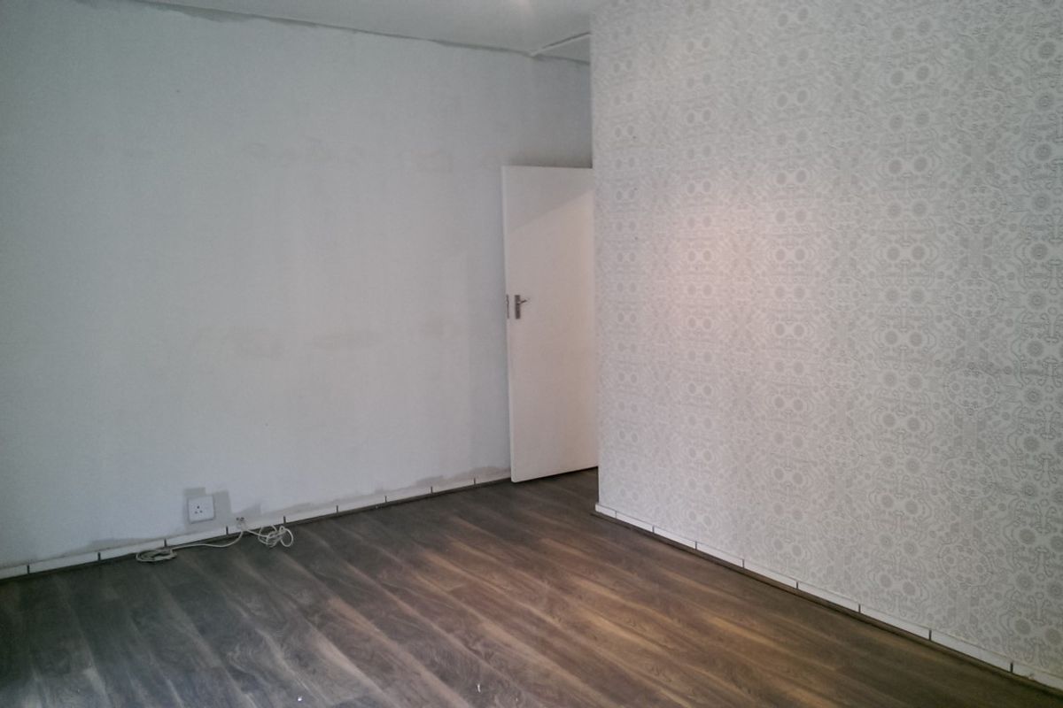 An empty office space featuring dark laminate flooring and a patterned feature wall, currently requiring finishing touches to the skirting and wall edges.