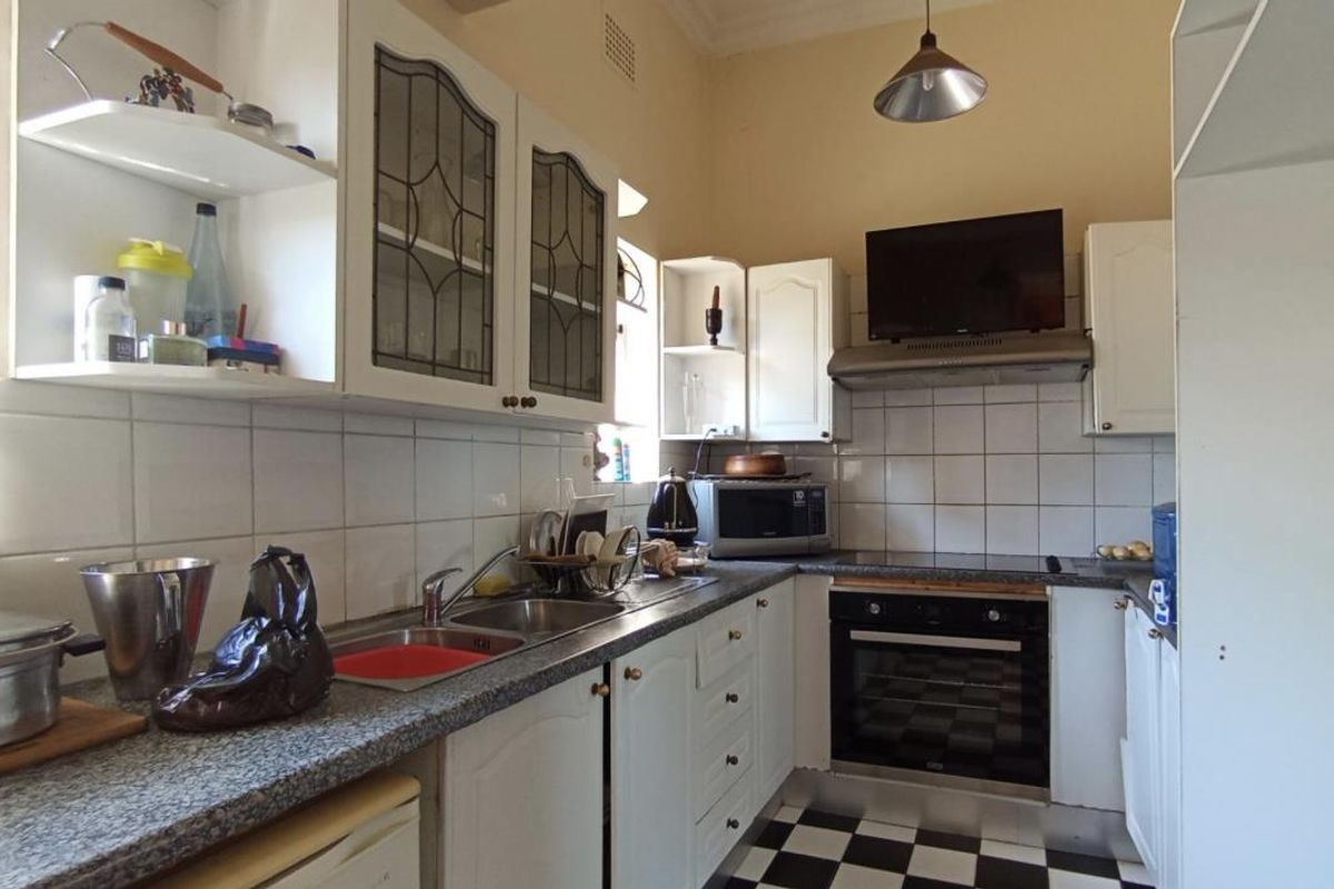 A functional kitchen featuring white cabinetry, granite-look countertops, a built-in oven with extractor fan, and classic black-and-white checkered floor tiles.