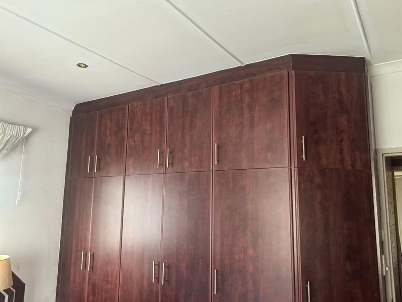Bedroom featuring floor-to-ceiling dark wood built-in cupboards with modern handles and recessed ceiling lighting.