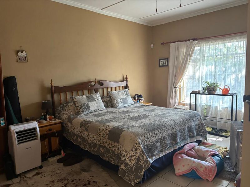 A spacious bedroom featuring tiled flooring, a ceiling fan, and large windows with curtain rods, offering a functional and comfortable living space.