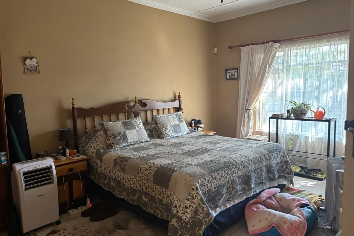 A spacious bedroom featuring tiled flooring, a ceiling fan, and large windows with curtain rods, offering a functional and comfortable living space.