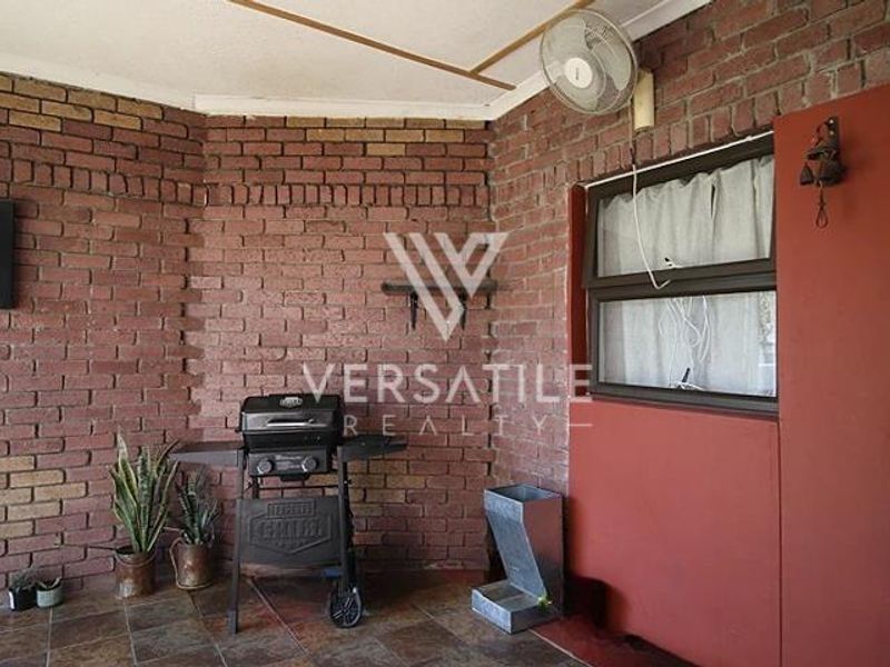 A covered patio area featuring exposed brick walls, tiled flooring, and a wall-mounted fan, offering a functional outdoor space for relaxation.