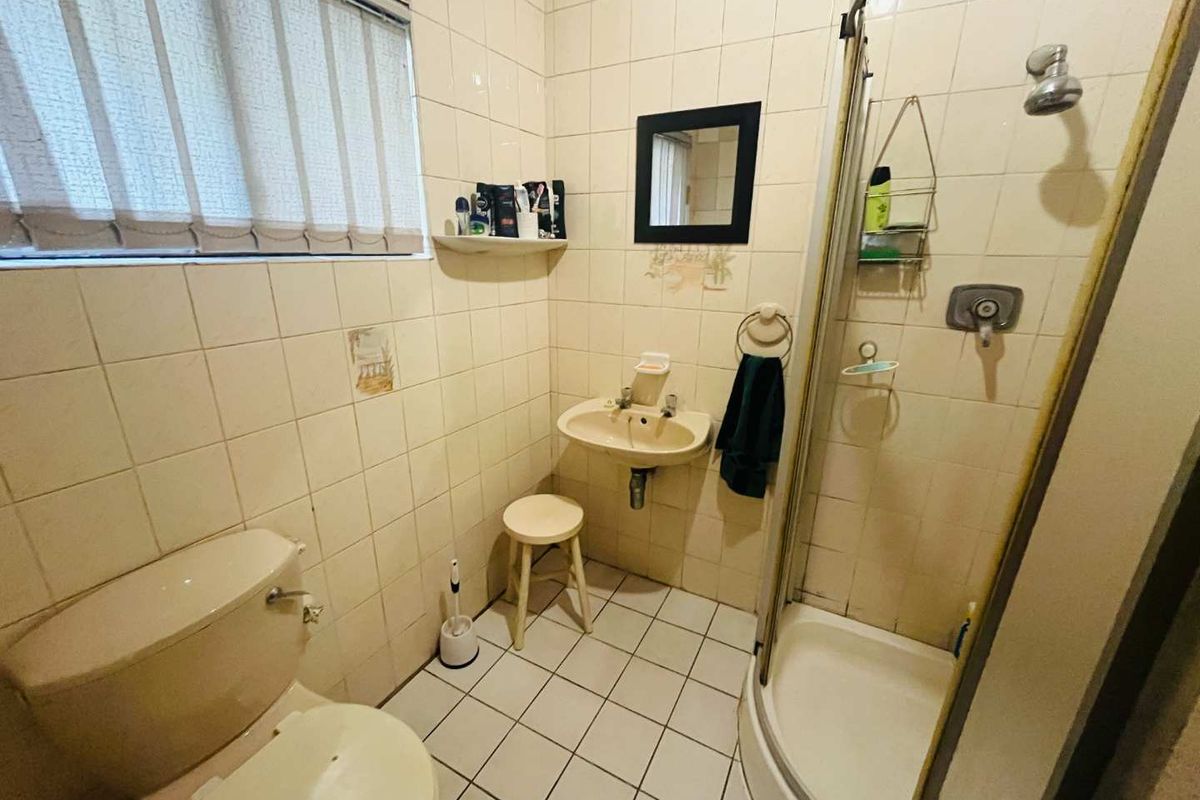 A compact bathroom featuring a corner shower enclosure, wall-mounted basin, and toilet with full-height wall tiling and a window.