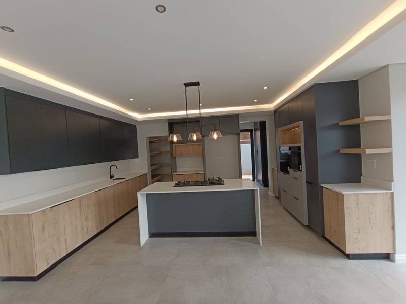 Modern, spacious kitchen featuring a central island with gas hob, sleek two-tone cabinetry, stone countertops, and integrated appliances with recessed ceiling lighting.
