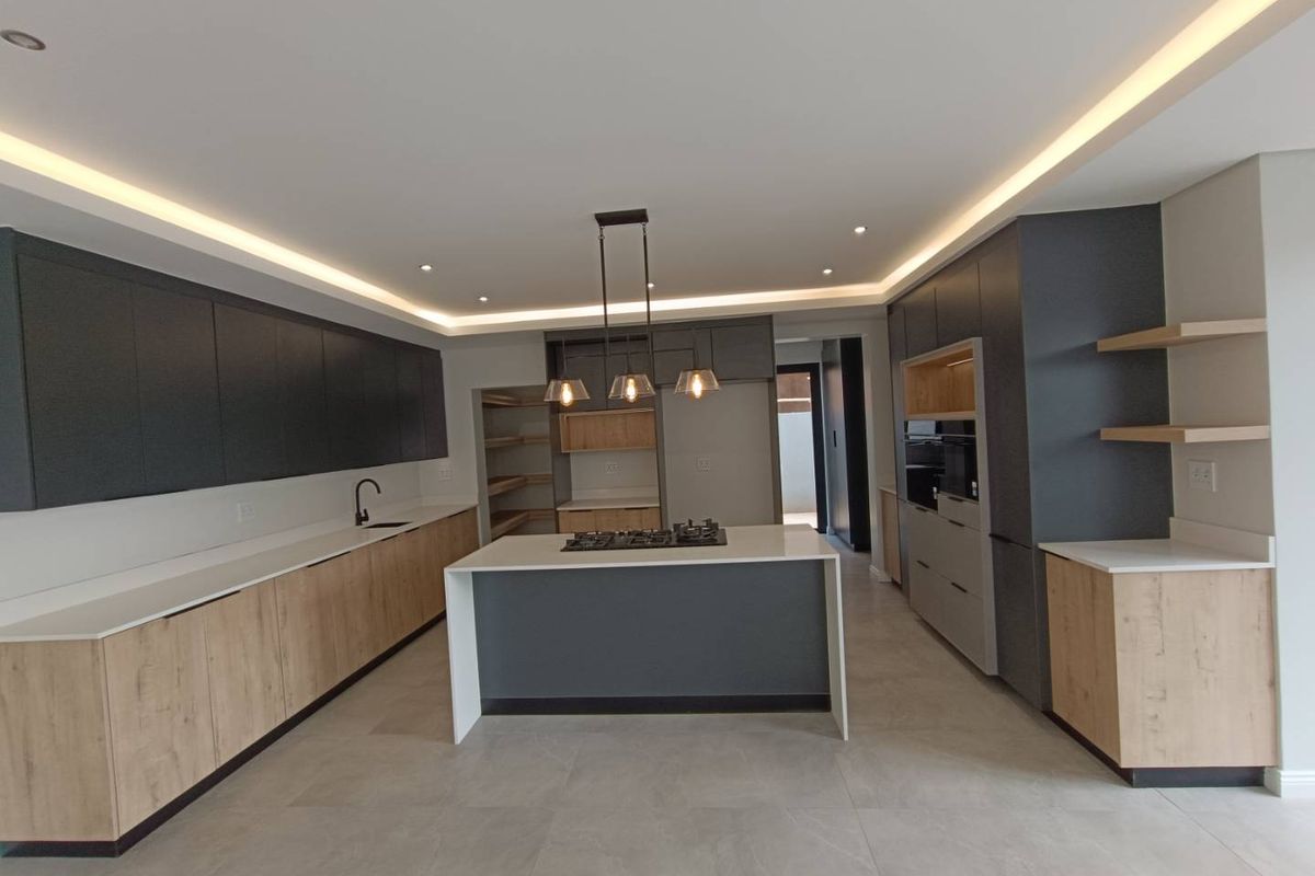 Modern, spacious kitchen featuring a central island with gas hob, sleek two-tone cabinetry, stone countertops, and integrated appliances with recessed ceiling lighting.