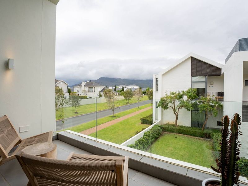 A modern balcony featuring a sleek glass balustrade and tiled flooring, offering pleasant views of the surrounding estate and mountain landscape.