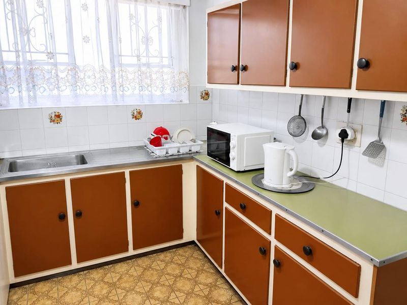 A dated kitchen featuring original laminate cabinetry, a stainless steel sink, and tiled splashbacks, offering significant potential for a modern renovation.