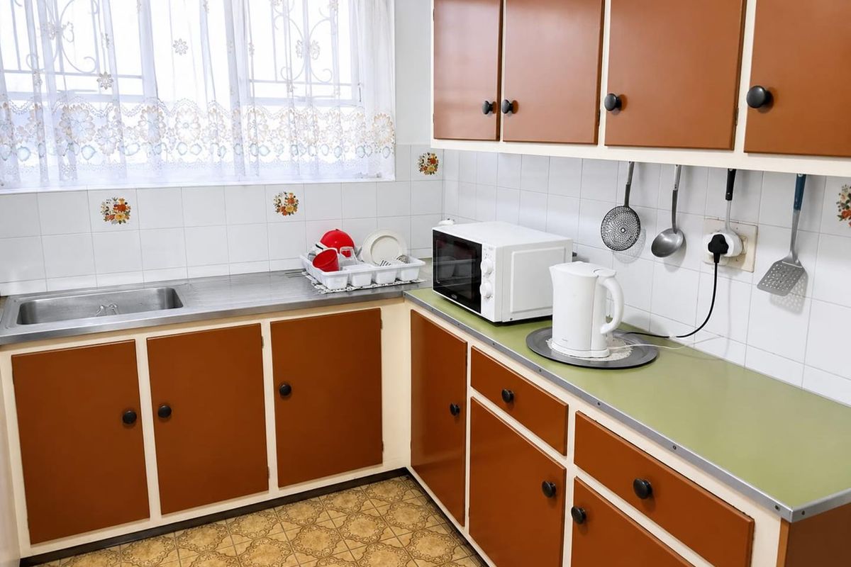 A dated kitchen featuring original laminate cabinetry, a stainless steel sink, and tiled splashbacks, offering significant potential for a modern renovation.