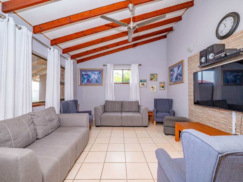 Spacious living room featuring exposed timber ceiling beams, a ceiling fan, tiled flooring, and a textured stone-cladding feature wall.