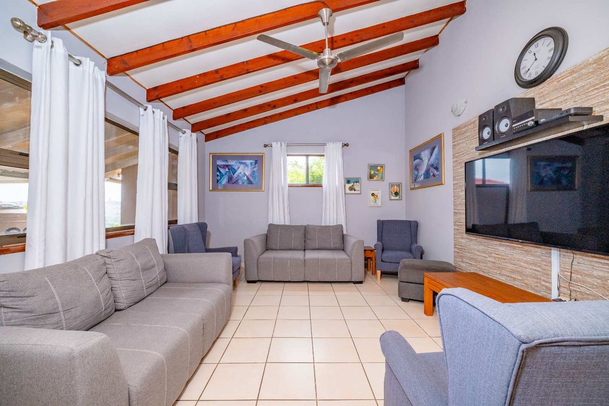 Spacious living room featuring exposed timber ceiling beams, a ceiling fan, tiled flooring, and a textured stone-cladding feature wall.