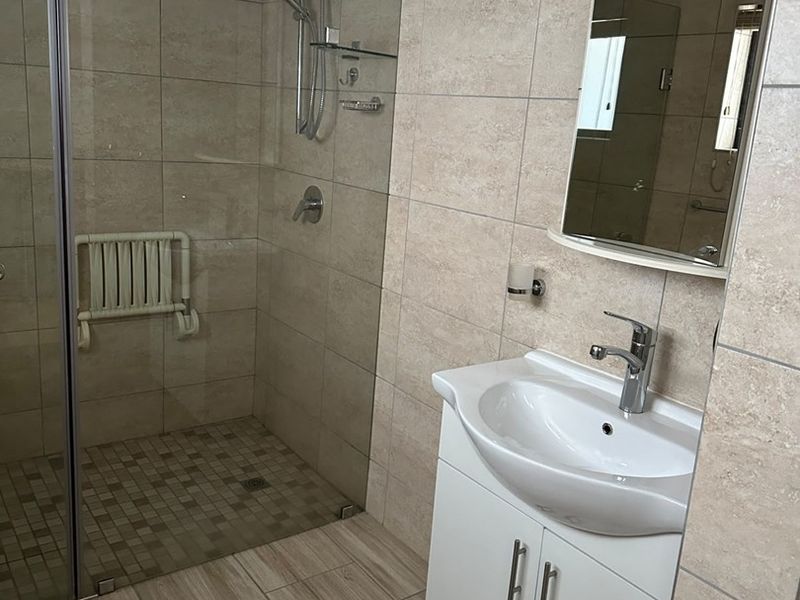 A modern, clean bathroom featuring a walk-in shower with a glass screen, wall-mounted shower seat, and a vanity unit with a basin.