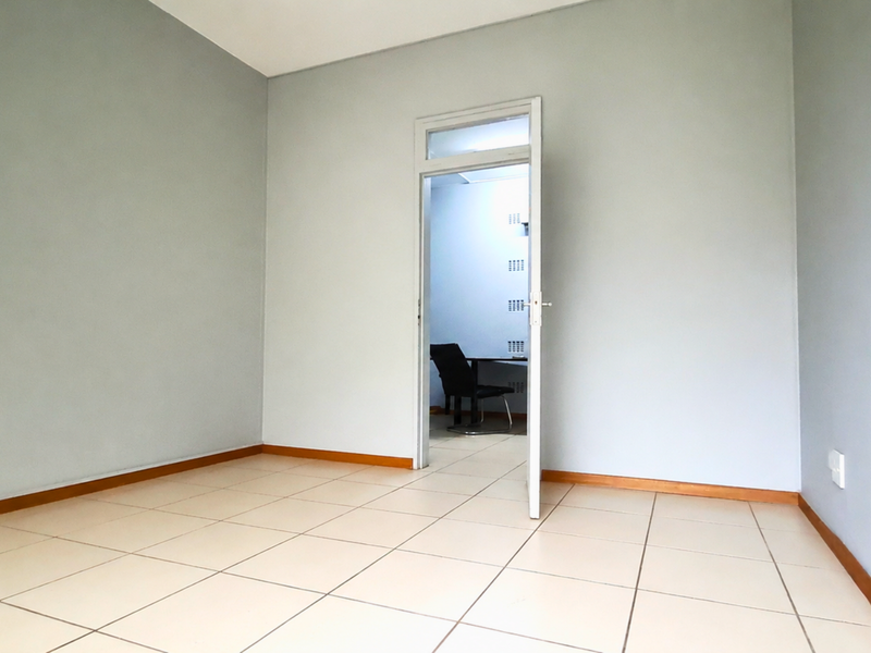A clean, empty office space featuring neutral wall paint, tiled flooring, and a doorway leading to an adjacent room.