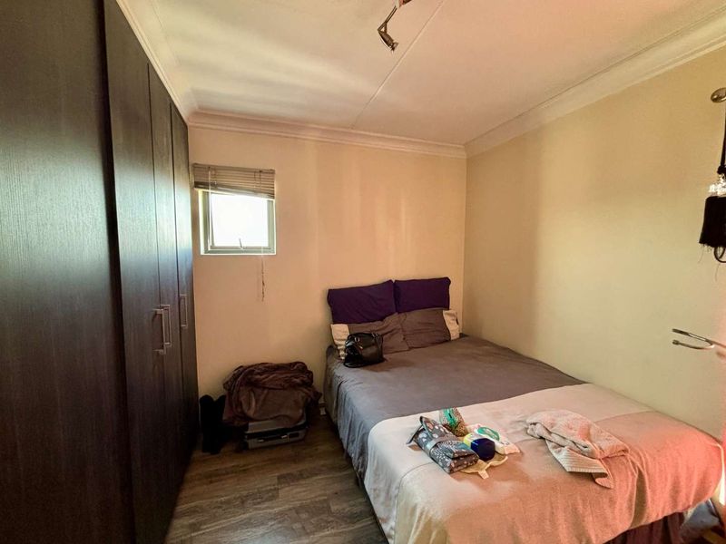 A compact bedroom featuring built-in dark wood cupboards, laminate flooring, and a small window, providing a functional sleeping space.