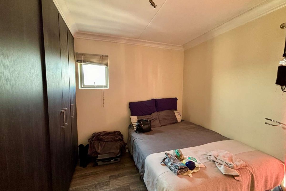 A compact bedroom featuring built-in dark wood cupboards, laminate flooring, and a small window, providing a functional sleeping space.