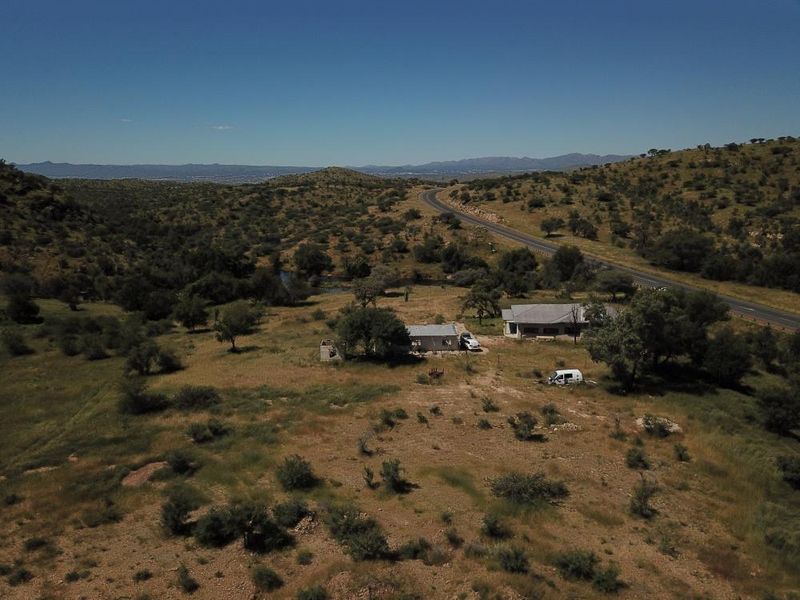Aerial view of a rural property featuring a main dwelling and outbuildings situated in a vast, open landscape near a regional road.