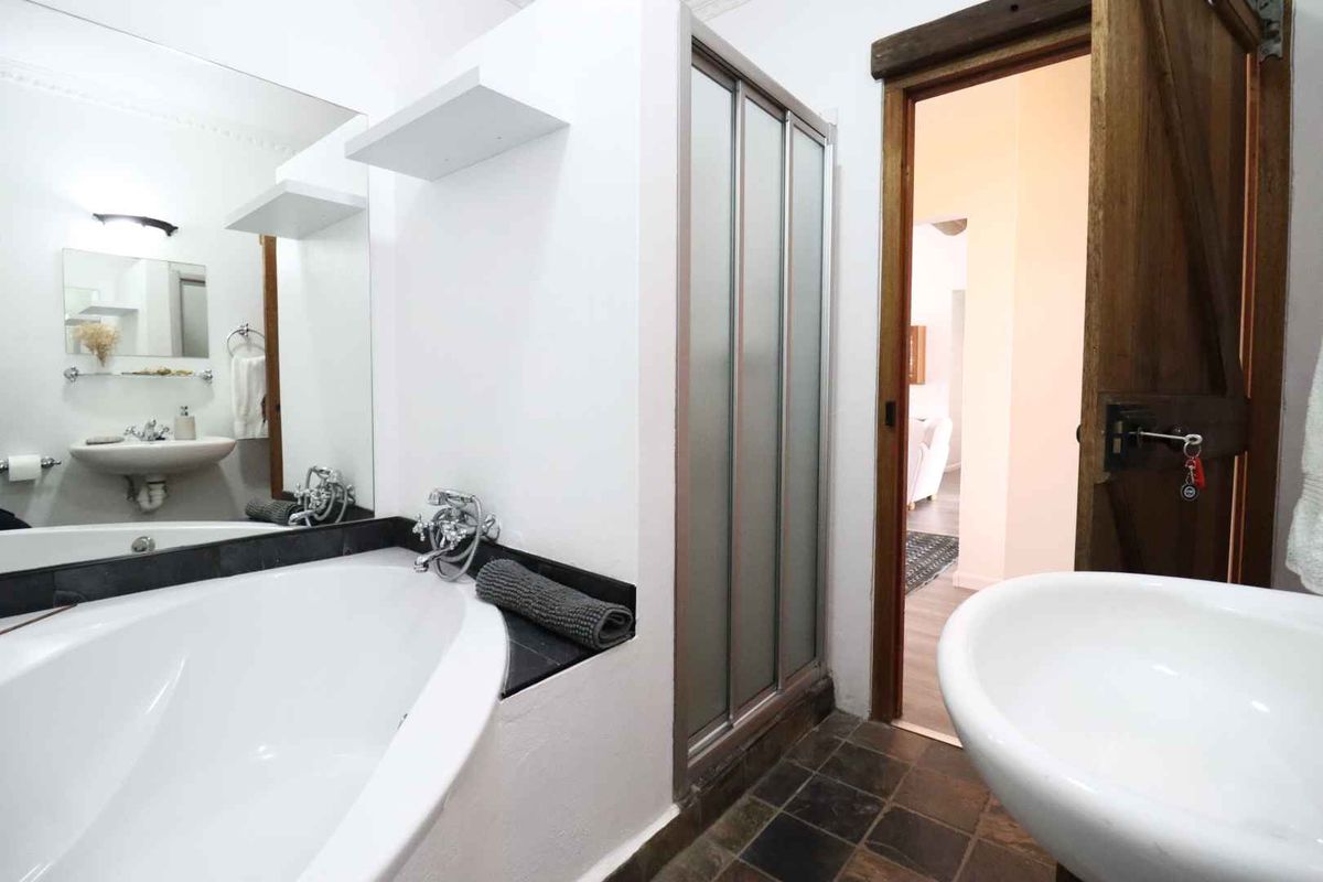 Bathroom featuring a built-in bathtub, separate shower enclosure, pedestal sink, and dark tiled flooring with a rustic timber door.