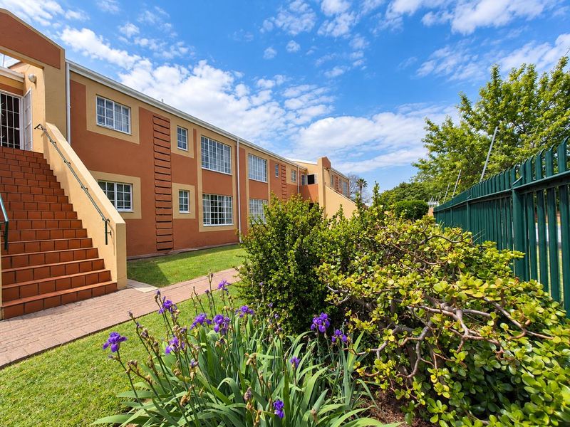 Exterior view of a townhouse complex featuring a tiled staircase, paved walkway, and well-maintained garden area with perimeter fencing.