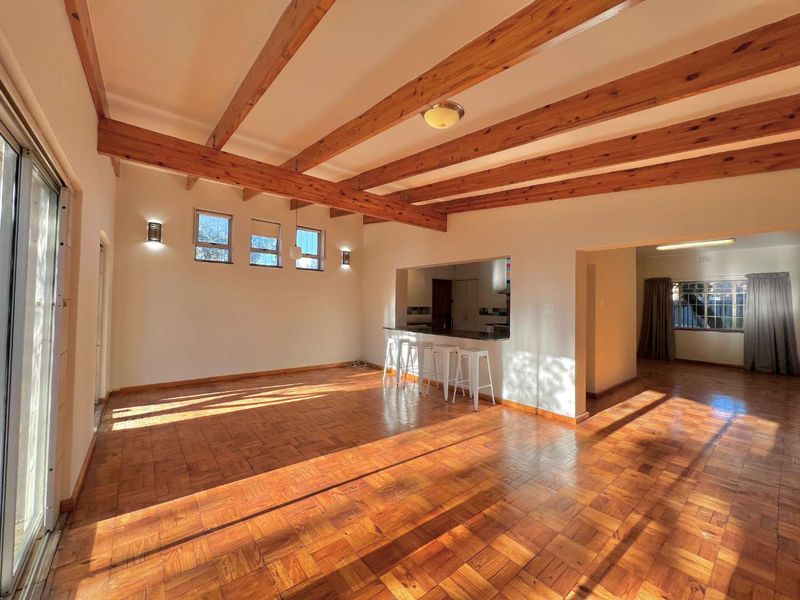 Spacious open-plan living area featuring warm parquet flooring, exposed timber ceiling beams, and a convenient serving hatch connecting to the kitchen.