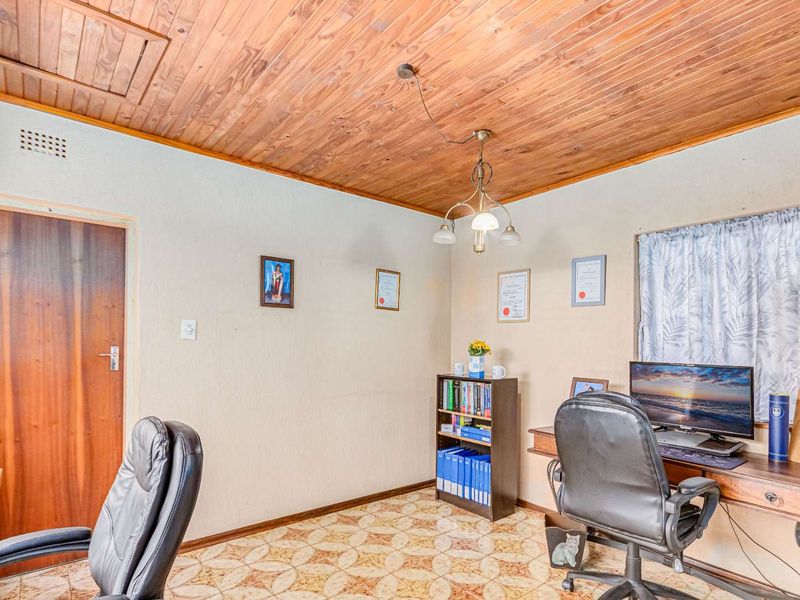 A functional home office space featuring a timber-clad ceiling, patterned vinyl flooring, and a standard interior door.