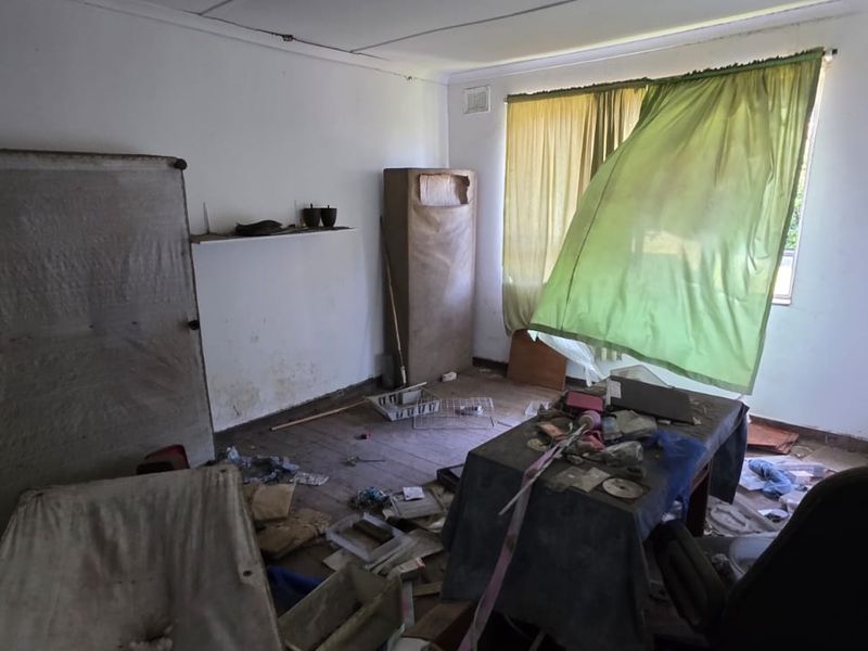 A bedroom in poor condition requiring significant renovation, featuring built-in storage and a window with natural light.