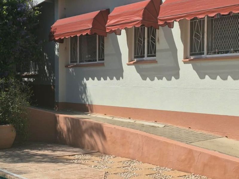 Exterior view of the pool area featuring a paved deck, retaining wall, and windows fitted with fixed red fabric awnings and security bars.