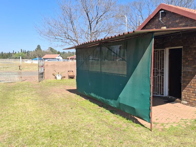 Rear view of a brick house featuring a covered patio area with shade cloth, a paved walkway, and a fenced garden.