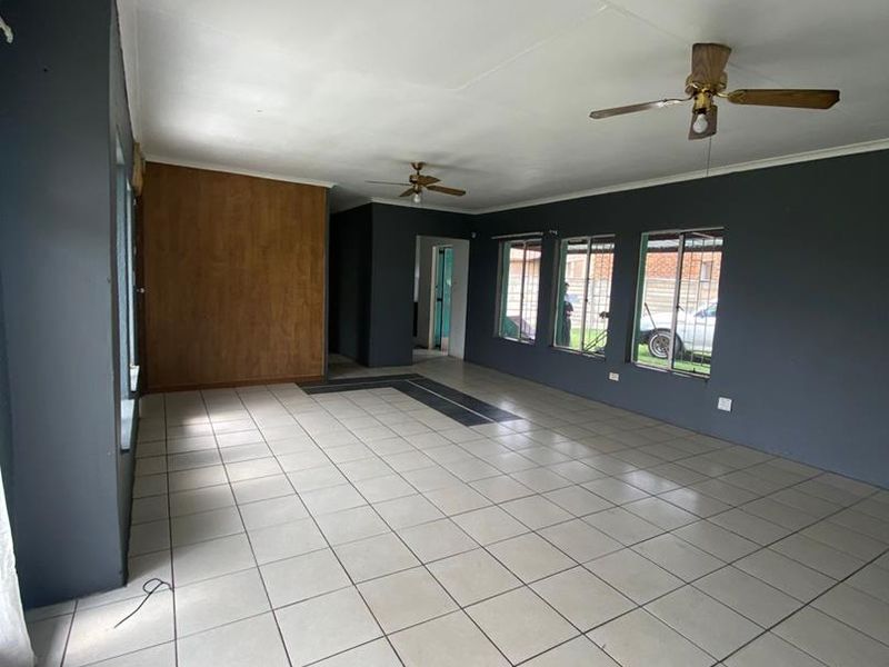Spacious, empty living area featuring neutral tiled flooring, ceiling fans, and dark grey accent walls with large windows providing natural light.