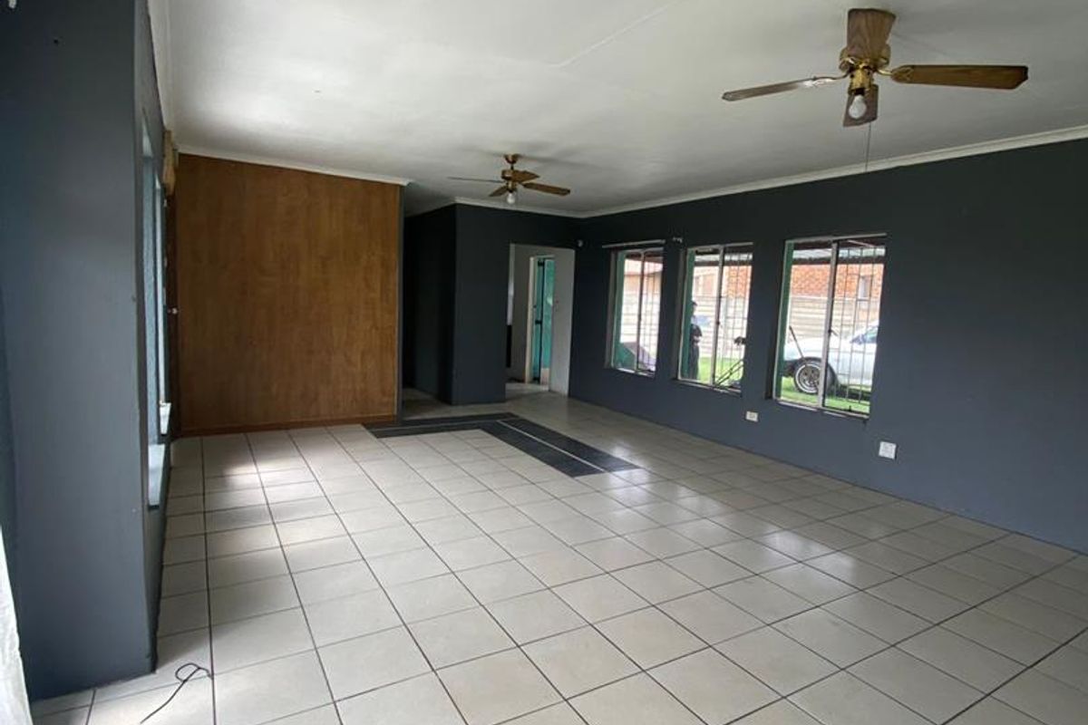 Spacious, empty living area featuring neutral tiled flooring, ceiling fans, and dark grey accent walls with large windows providing natural light.