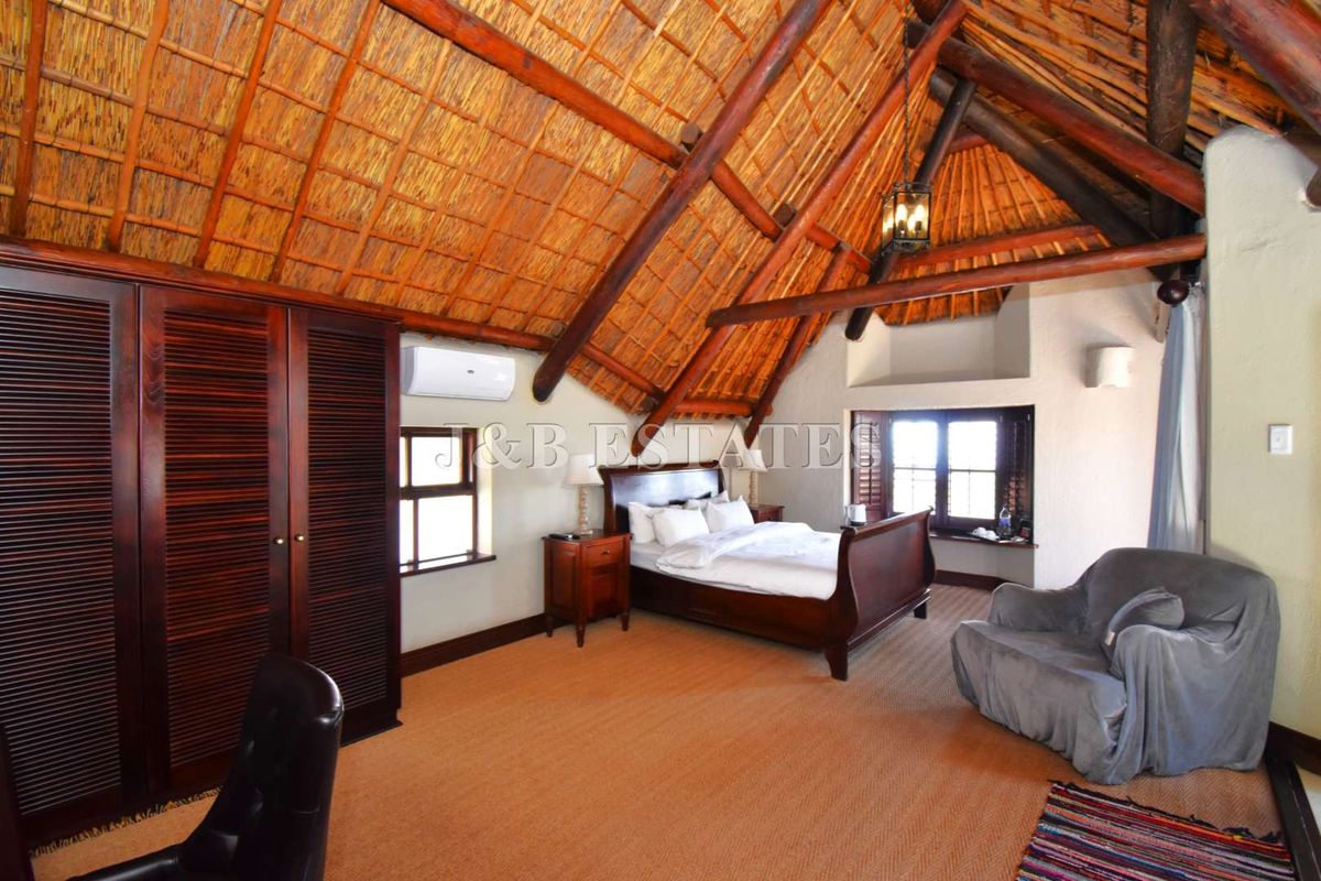 Spacious bedroom featuring a high vaulted thatched ceiling with exposed timber beams, built-in wooden cabinetry, and an integrated air conditioning unit.