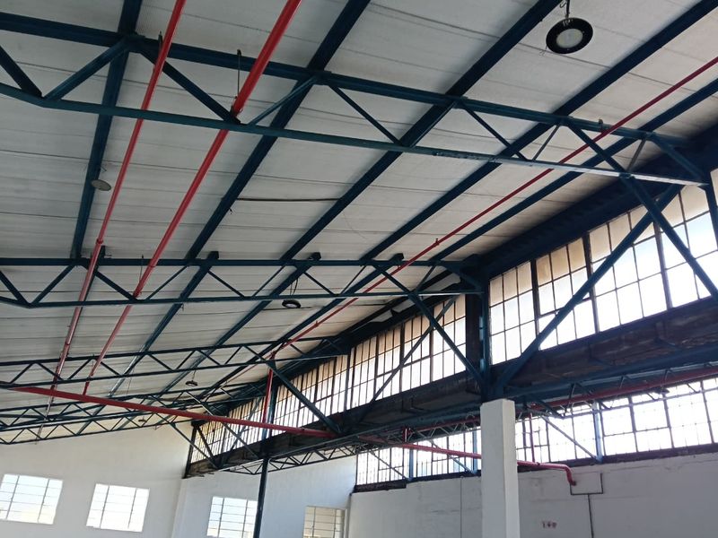 Spacious industrial utility area featuring high exposed steel roof trusses, fire sprinkler systems, and large clerestory windows providing ample natural light.