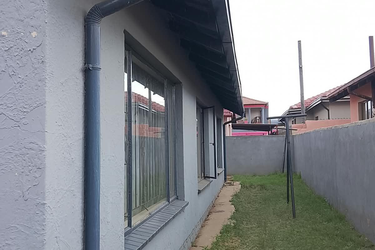 Side view of the property showing the exterior wall, downpipe, guttering, and a narrow grassed area enclosed by a boundary wall.