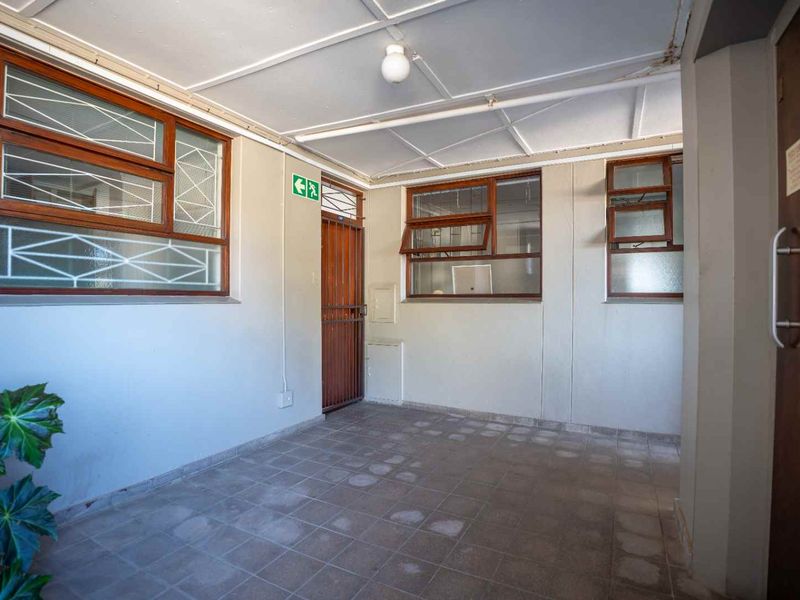 A functional entrance area featuring tiled flooring, timber-framed windows, and a security gate, providing a secure and practical access point to the apartment.