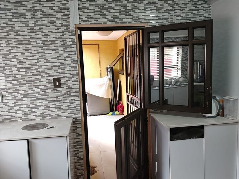 A functional scullery area featuring mosaic tile backsplashes, built-in cabinetry, and tiled flooring, currently requiring minor finishing touches to the door frame and cabinetry.