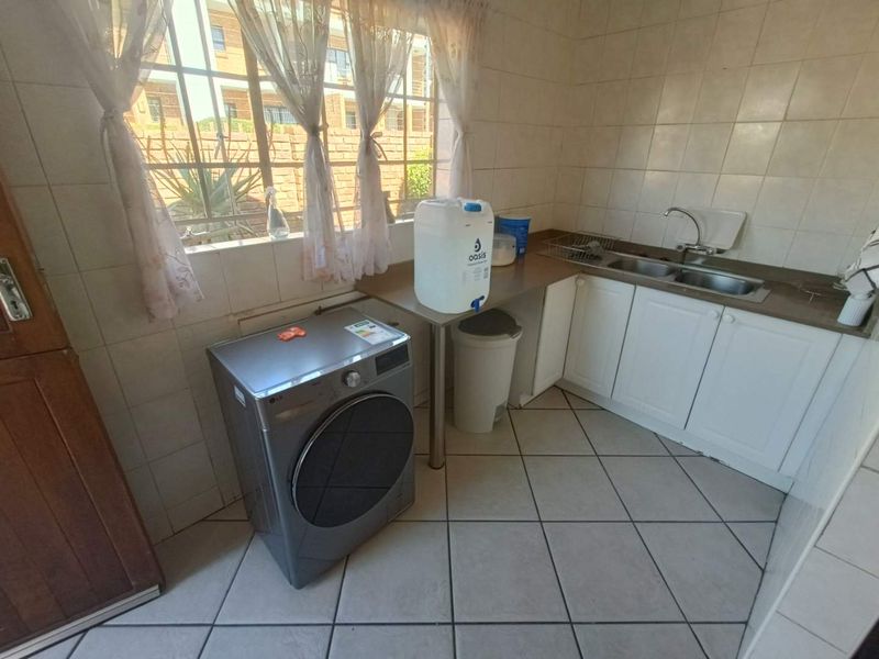 A functional laundry area featuring tiled flooring, a double basin sink, built-in cabinetry, and a window with security bars.