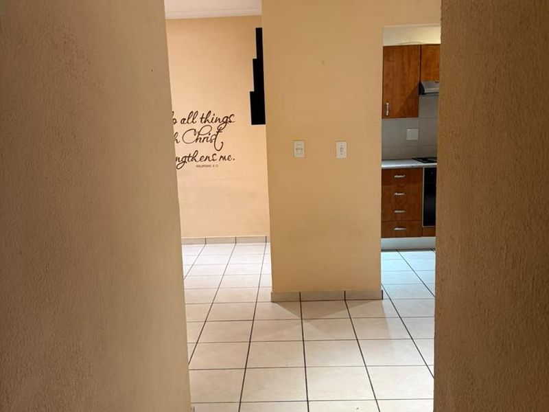 A view through a hallway leading into an open plan living area and kitchen with tiled flooring and recessed lighting.