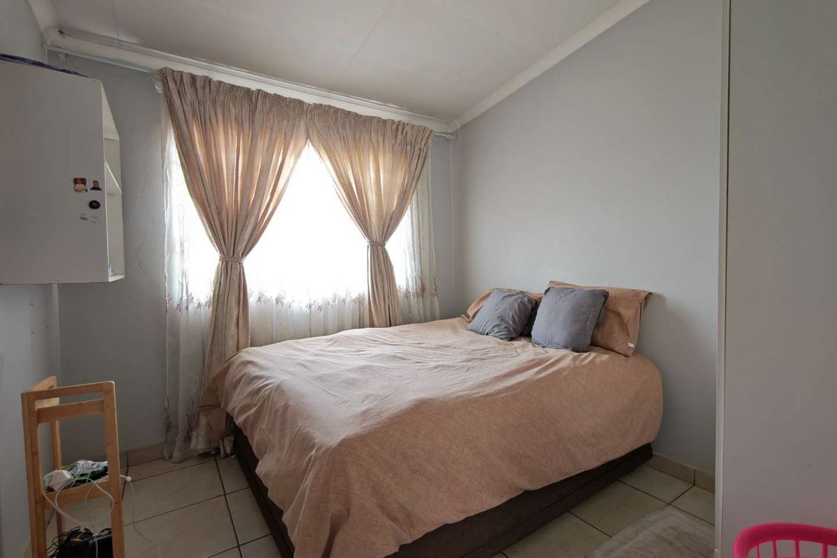 A functional bedroom featuring tiled flooring, a window with curtain fixtures, and built-in storage space.