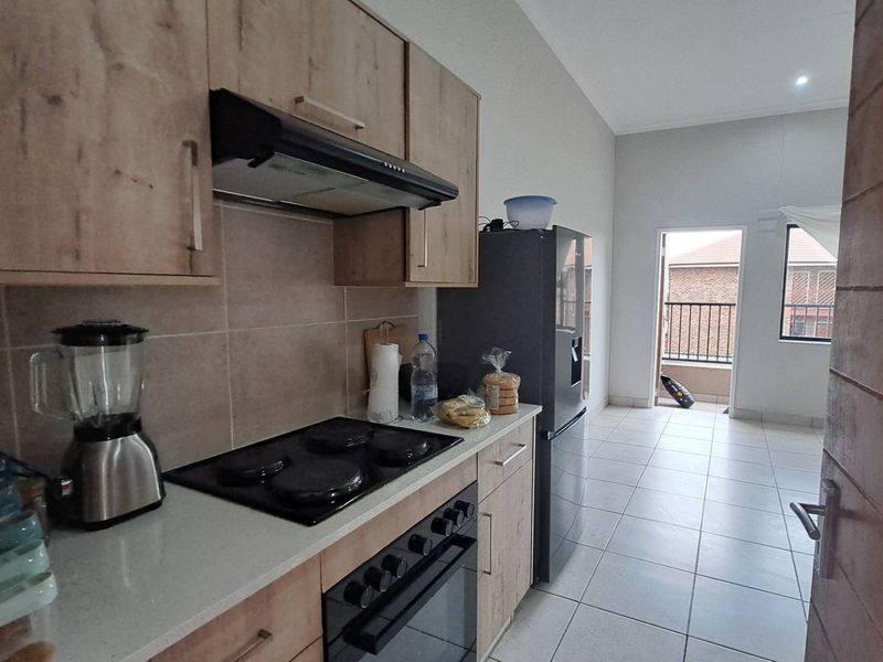 A functional kitchen featuring light wood-finish cabinetry, a built-in electric oven and hob, extractor fan, and tiled flooring, with direct access to a balcony.