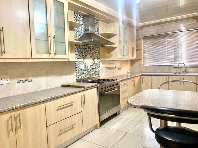 A functional kitchen featuring light wood cabinetry, stainless steel appliances, a tiled backsplash, and ample countertop space with a breakfast nook area.
