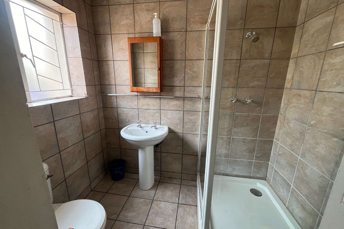 A functional bathroom featuring a pedestal basin, a shower enclosure with a glass door, and full-height wall tiling.