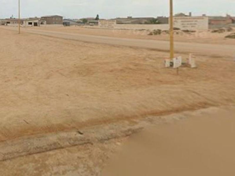A view of an unpaved residential street with utility poles, showing the surrounding vacant land and neighborhood context.