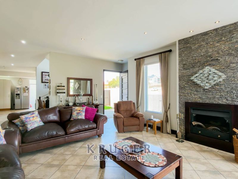 Spacious open-plan living area featuring a prominent stone-clad fireplace, tiled flooring, and recessed downlighting, creating a warm and inviting atmosphere.