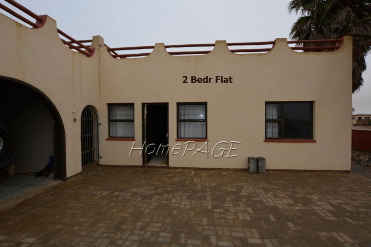 Exterior view of the property featuring a paved courtyard, arched entryway, and a flat-roofed facade with decorative parapet detailing.