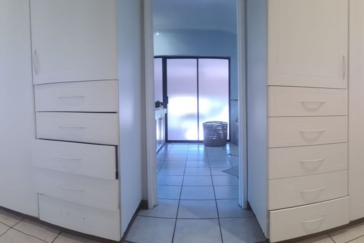 Bedroom featuring built-in cupboards and tiled flooring, leading through to an adjacent space with a sliding door.